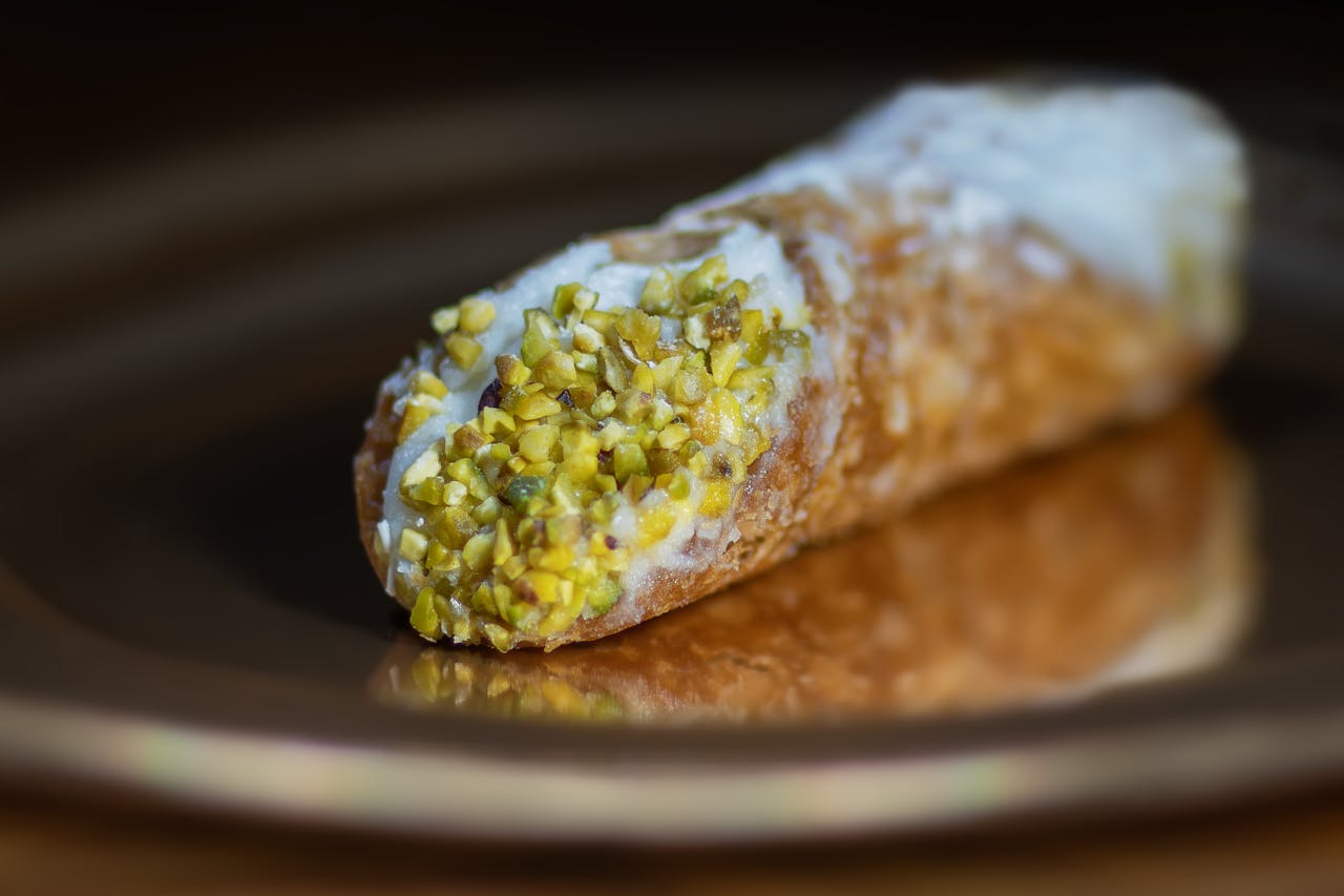 about-us-01 Close-up of a pistachio-topped cannoli pastry, showcasing the texture and vibrant colors.